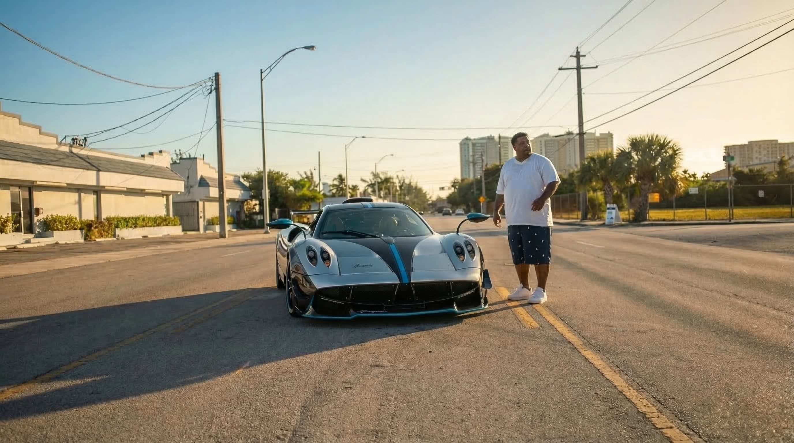 Pagani Huayra prateado em uma rua urbana com um homem ao lado no entardecer.